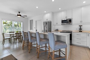 Une cuisine moderne avec des meubles blancs, des appareils en acier inoxydable et un coin repas comprenant des chaises et une table en bois.