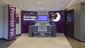 Un comptoir d’accueil d’hôtel avec une enseigne « Premier Inn », une enseigne « Garantie d’une bonne nuit » et une enseigne « Enregistrement ».