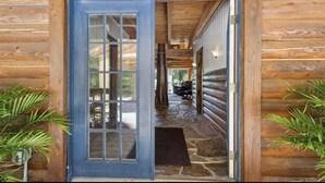 Una cabaña de madera con puerta azul, acceso empedrado y porche cubierto.