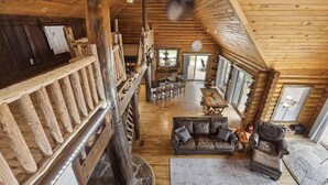 Interior espacioso de una cabaña de troncos, con techo alto, comedor y zona de estar acogedora.