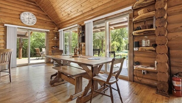 Interior rústico de una cabaña de madera, con una mesa y sillas de madera, y un ventanal grande.