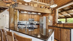 Una cocina rústica con gabinetes de madera, encimera de granito, electrodomésticos de acero inoxidable y una isla grande con taburetes de bar.