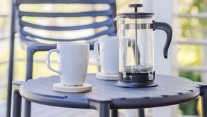 Uma prensa francesa para café sobre uma mesa com duas xícaras brancas.