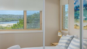 Ein Schlafzimmer mit Bett, Nachttisch, Lampe und Blick auf einen Strand durch ein Fenster.