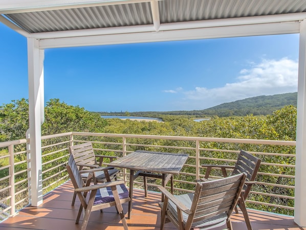 A covered outdoor seating area with a table and chairs, overlooking a scenic landscape with hills and a body of water. - 2 Bedroom Estuary Water View Apartment at Hastings Cove! (Tweed)