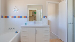 Ein Badezimmer mit Waschbecken, Spiegel und Badewanne. Eine Tür führt in einen anderen Raum.