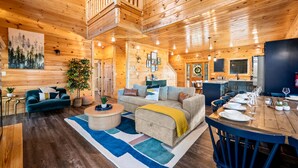 Eine geräumige Holzhütte mit Essbereich, einem Wohnzimmer mit Sofa und Couchtisch sowie einer Treppe, die in eine obere Ebene führt.