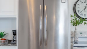 A stainless steel refrigerator with a freezer compartment below, white cabinetry, and a clock on the wall. - Charming Midtown Tulsa Home Steps From Expo Square.  (Tulsa)