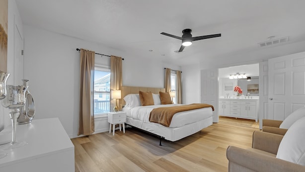 A modern bedroom with a bed, bedside tables, a ceiling fan, and a view of the city through the window. - Charming Midtown Tulsa Home Steps From Expo Square.  (Tulsa)
