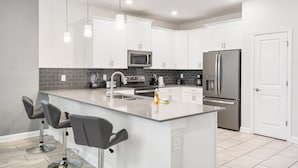 A modern kitchen with white cabinets, stainless steel appliances, and a central island with bar stools.
