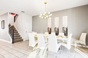 A modern dining area with a staircase, white chairs, and a chandelier. - Epic Themed Game Room & Theater Near Disney Parks (Kissimmee)