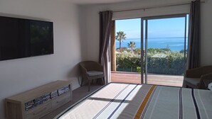Ein Schlafzimmer mit einem großen Bett, einem an der Wand montierten Fernseher, einer Holzeinrichtung mit DVDs, einem Sessel und einem Balkon mit Meerblick.