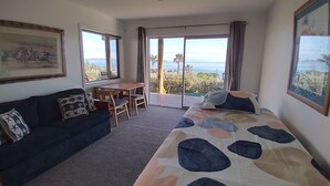 Ein Schlafzimmer mit Bett, einer Couch, einem Schreibtisch und Blick ins Freie.