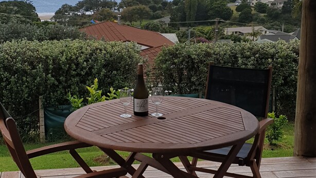 Eine Holzterrasse mit rundem Tisch und zwei Stühlen, mit Blick auf eine Küstenlandschaft mit Häusern und Bäumen.