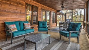 Eine Holzterrasse mit überdachter Sitzgruppe, inklusive zwei Sofas, einer Bank, einem Tisch und einem Esstisch mit Stühlen.