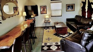 Una sala de estar con una mesa de comedor de madera, un sofá de cuero y una alfombra estampada.