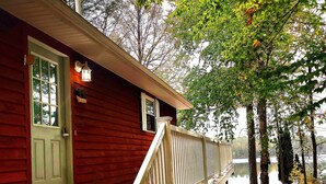 A red cabin with a white staircase leading to a porch, surrounded by autumn leaves and trees.