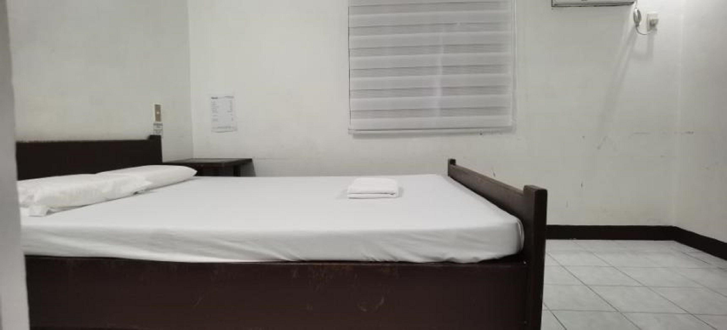 Habitación individual con una cama de una sola plaza, cabecera de madera, colchón blanco y mesita de noche pequeña.