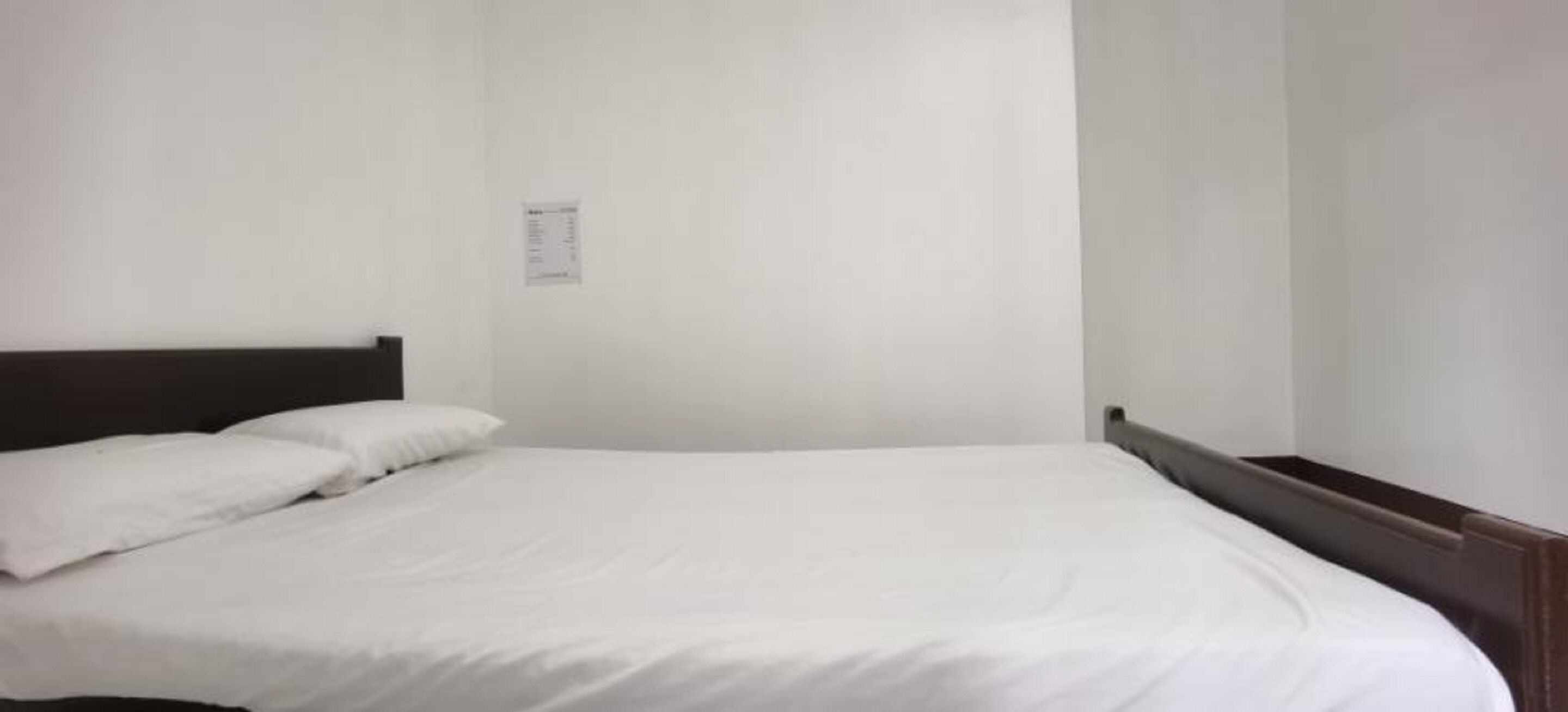 A single bed with white bedding in a room with plain white walls and a dark headboard.