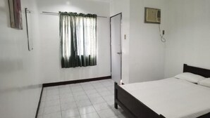 Un dormitorio con cama, ventana con cortinas, radiador y puerta.