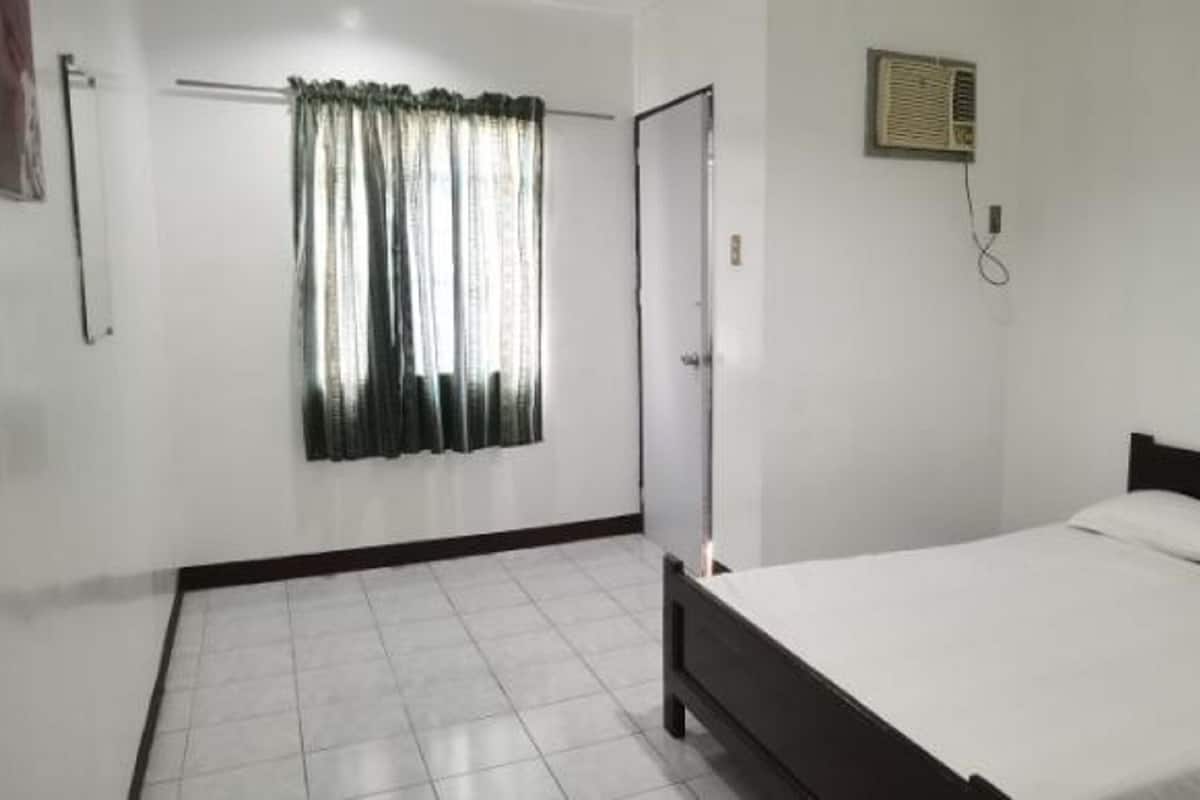 A bedroom with a bed, a window with curtains, a radiator, and a door.