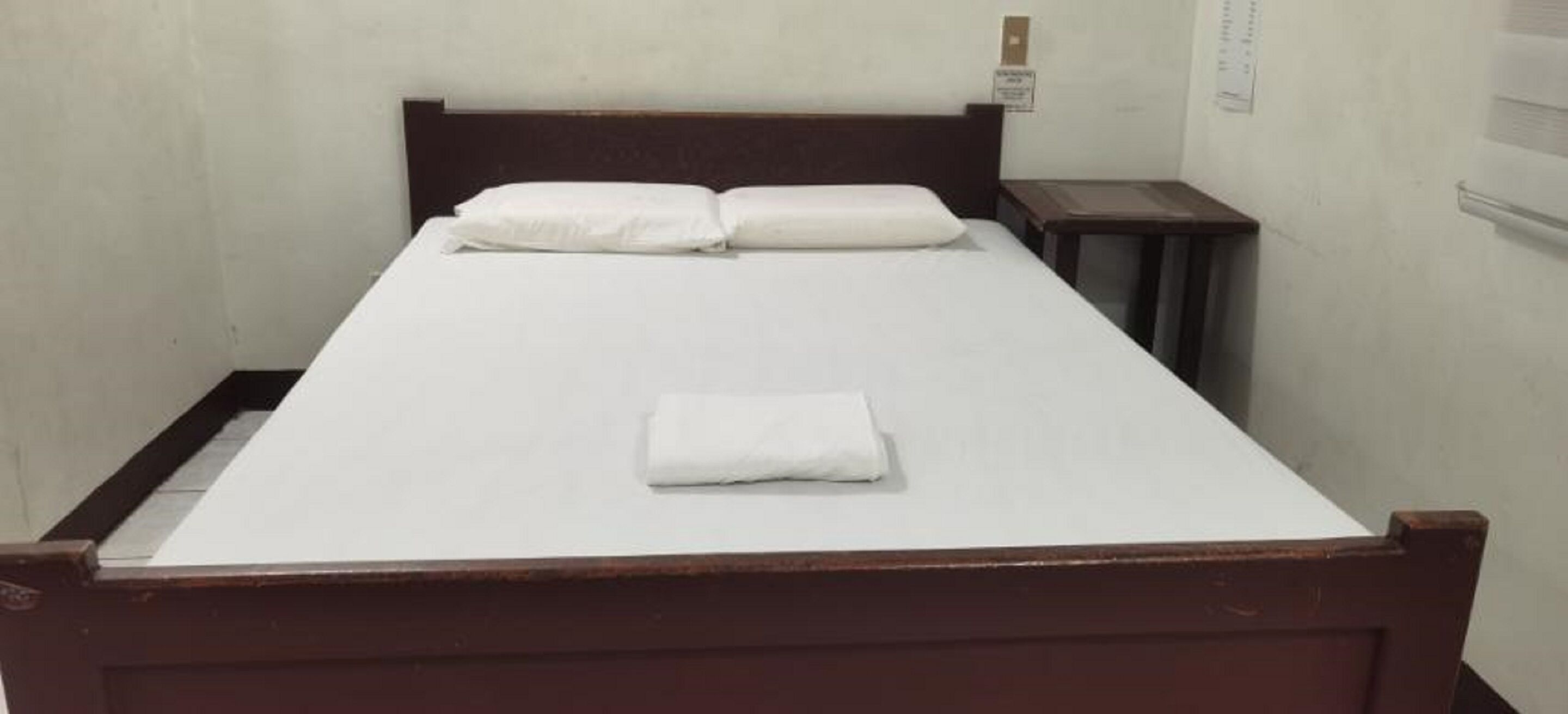 Una cama individual con estructura de madera, ropa blanca de cama y una toalla blanca doblada sobre la cama.
