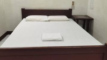 Una cama individual con estructura de madera, ropa blanca de cama y una toalla blanca doblada sobre la cama.