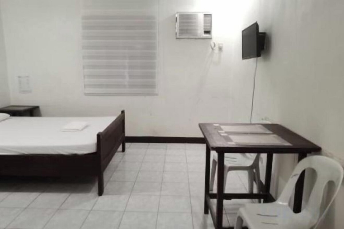 Una habitación con cama, escritorio, silla y ventana con persianas.