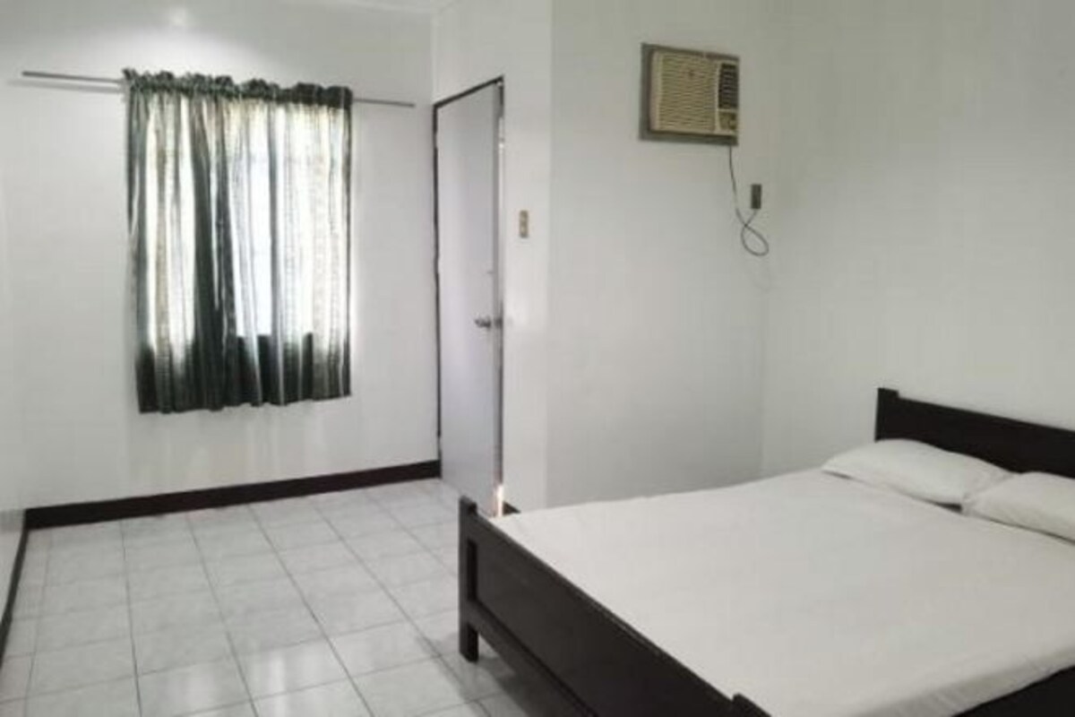 Quarto com cama, cortina, porta e ar-condicionado fixado na parede.