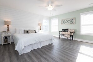 Une chambre à coucher avec un lit, des tables de chevet, un ventilateur de plafond et une fenêtre avec des stores.