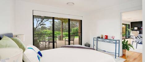 A bedroom with a large bed, a glass door leading to an outdoor deck, and a small table with decorative items.