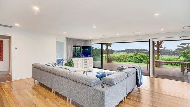 Una sala de estar moderna con un sofá gris, un televisor de pantalla plana y un amplio ventanal corredero que da a una terraza exterior.