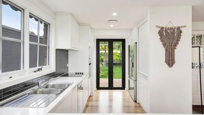 Una cocina moderna con muebles blancos, salpicadero de azulejos negros, electrodomésticos de acero inoxidable y suelo de madera.
