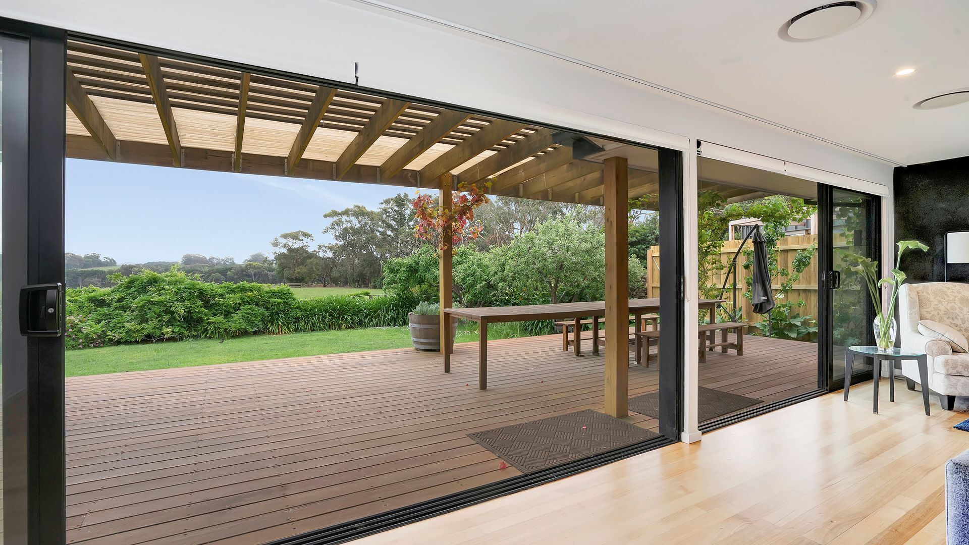 A modern house with a wooden deck, a covered outdoor seating area, and a glass door leading to a garden.