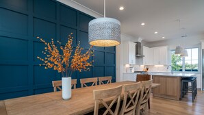 Een moderne keuken met witte kasten, een houten eettafel en een vaas met oranje bloemen.