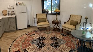 Una habitación con alfombra redonda, dos sillones, una mesita, una ventana y un refrigerador.
