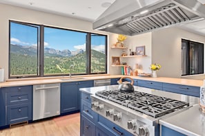 A modern kitchen with a large window, stainless steel appliances, and a view of mountains.