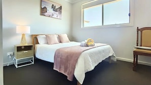A bedroom with a bed, a nightstand, a lamp, a chair, and a window. - Delightful 2-level home in Bardia (Bardia)