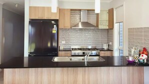 A modern kitchen with a black countertop, stainless steel appliances, wooden cabinets, and pendant lighting. - Delightful 2-level home in Bardia (Bardia)