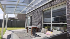A covered patio with a glass roof, a brick exterior, and a seating area with cushions and a small table. - Delightful 2-level home in Bardia (Bardia)
