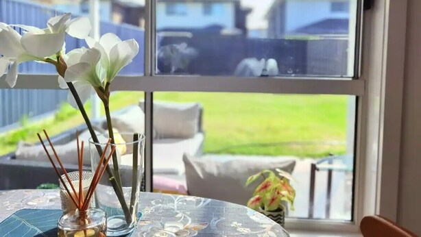 A room with a large window, a table with a vase of flowers, and a view of the outside. - Delightful 2-level home in Bardia (Bardia)