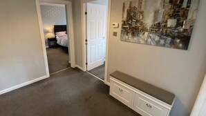 A hallway with a white door, a bench, and a cityscape painting on the wall. - NEW Super 2 Bedroom Flat in Falkirk (Falkirk)