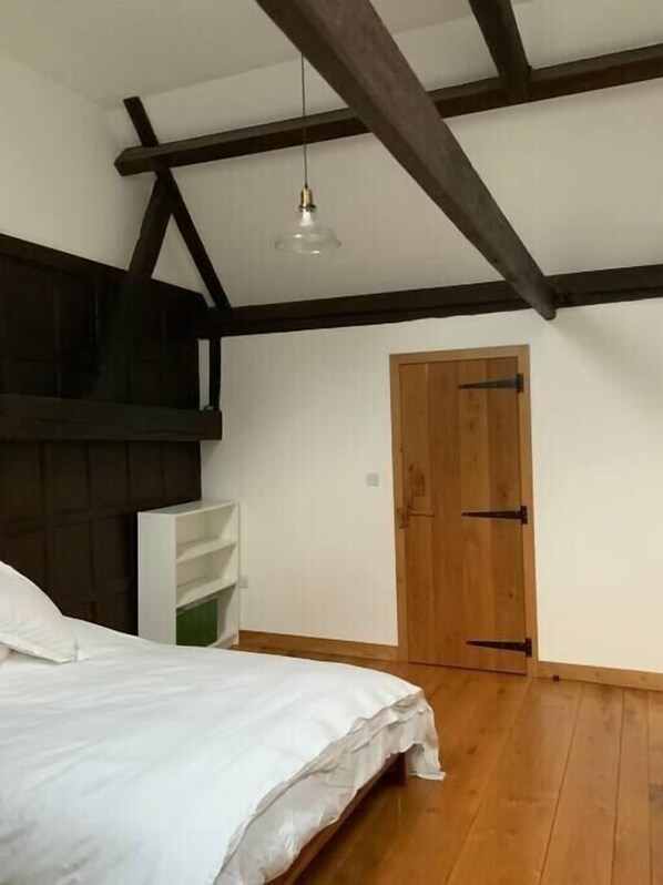 Une chambre avec un plafond en bois, un lit blanc, une porte en bois et une étagère blanche.
