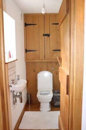 A small bathroom with wooden cabinets, a white sink, and a toilet. - Delightful 4BD Home full of Flair Edenbridge Kent (Dormansland)