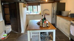 Een rustieke keuken met een houten tafel, stenen vloer en een inbouwplank.