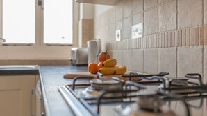 Une cuisine équipée d’une cuisinière à gaz, d’une planche à découper en bois et d’un panier de fruits contenant des bananes et une courge.