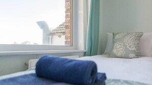 Un lit avec une serviette bleue, un oreiller à motifs et une vue sur un immeuble par la fenêtre.