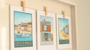 Trois affiches encadrées, ornées d’illustrations de bâtiments et de textes, sont accrochées à un mur.