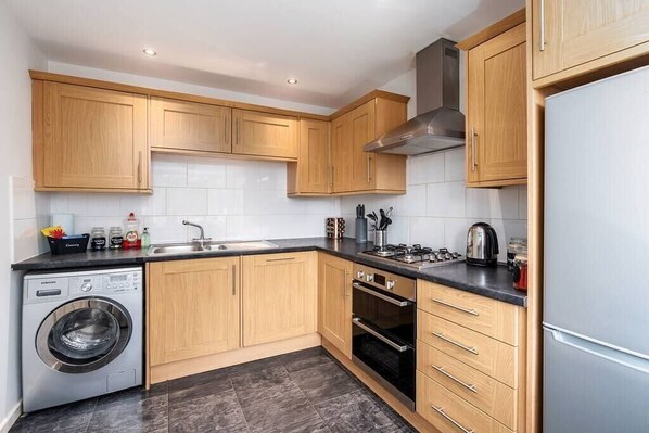 Una cocina moderna con armarios de madera, lavadora integrada, estufa y refrigerador.