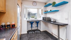 A modern kitchen with a window, two blue bar stools, a microwave, and jars of condiments. - Stunning 3 Bedroom Home Hillsborough Sheffield (Hillsborough)